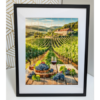 A vibrant jigsaw puzzle framed in a sleek black photo frame, depicting a picturesque vineyard scene with lush green vines, a stone building in the background, and baskets of grapes in the foreground.